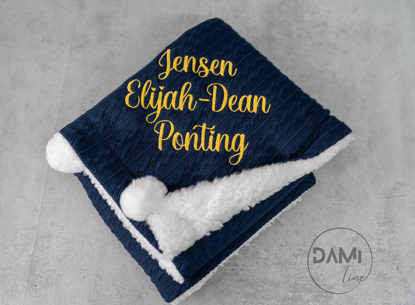 Personalised knitted baby blanket with white sherpa lining and 2 pom-poms.