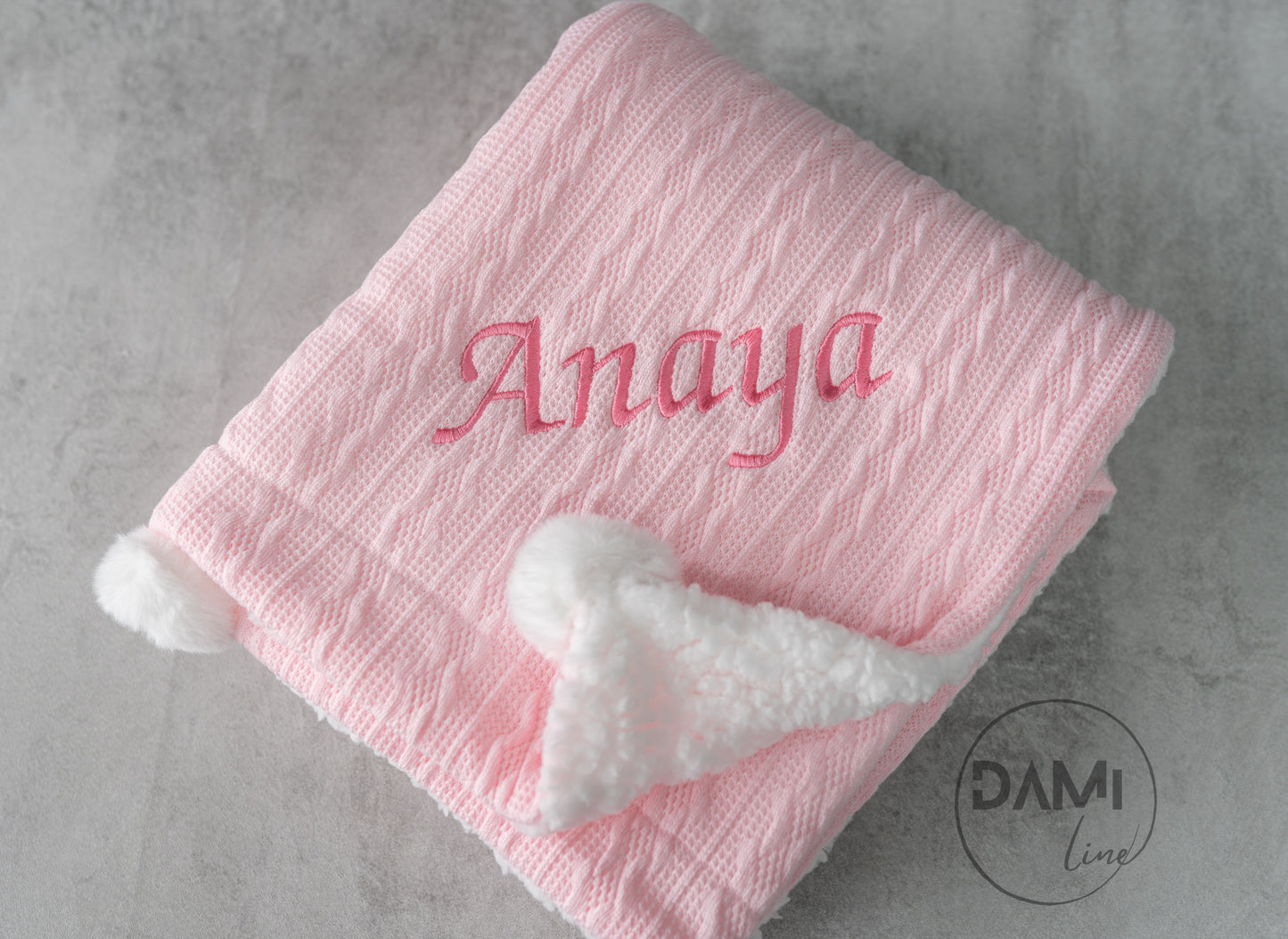Personalised knitted baby blanket with white sherpa lining and 2 pom-poms.