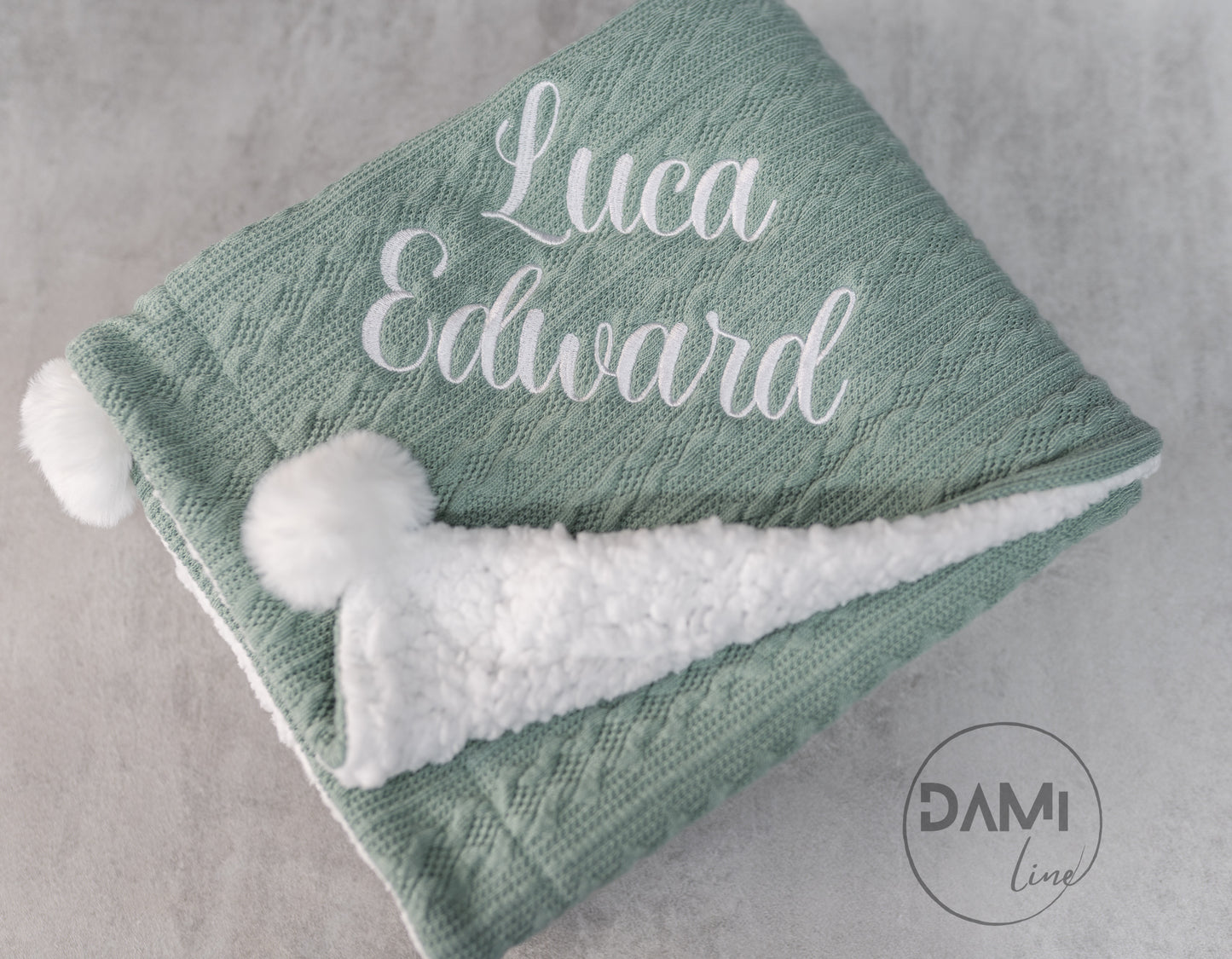 Personalised knitted baby blanket with white sherpa lining and 2 pom-poms.
