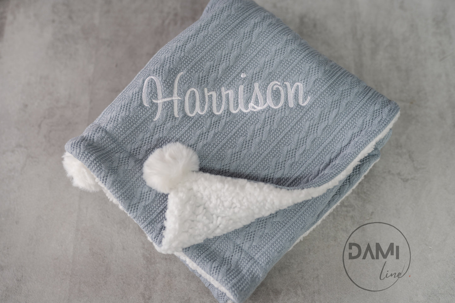 Personalised knitted baby blanket with white sherpa lining and 2 pom-poms.