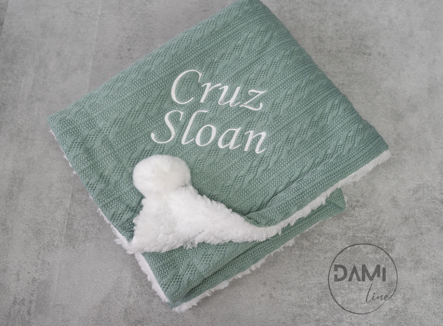 Personalised knitted baby blanket with white sherpa lining and 2 pom-poms.