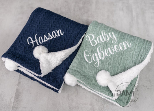 Personalised knitted baby blanket with white sherpa lining and 2 pom-poms.